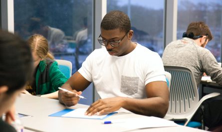 man in white crew neck t shirt sitting on chair while holding white pen