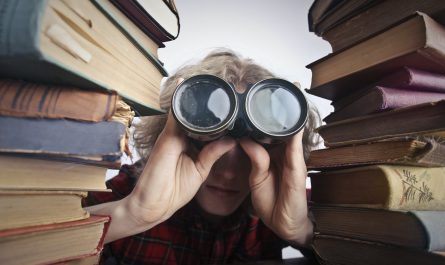 anonymous person with binoculars looking through stacked books