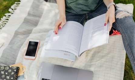 crop university student reading textbooks on green campus lawn